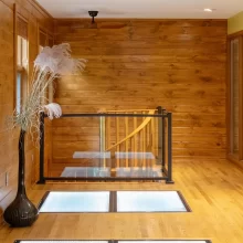 Loft landing with warm wood walls, wood flooring, glass floor panels, black railing, and spiral staircase below