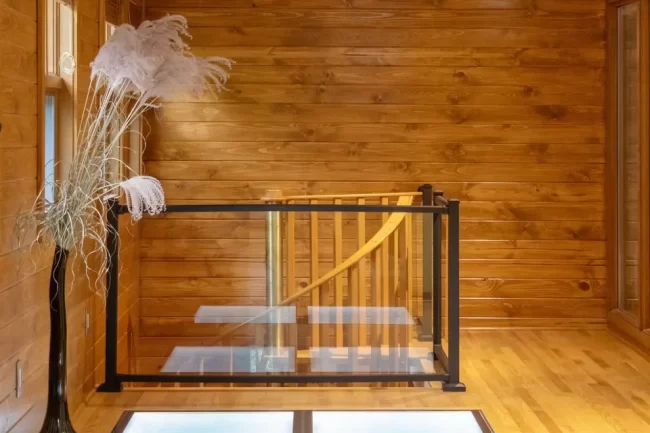 Loft landing with warm wood walls, wood flooring, glass floor panels, black railing, and spiral staircase below