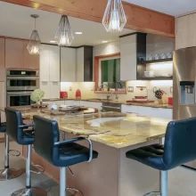Modern kitchen with light wood cabinetry, large stone island, pendant lights, stainless steel refrigerator, and built-in appliances