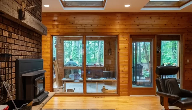 Wood Living Room with Glass Doors | Pennings & Sons Wood-paneled living room with brick fireplace, wood stove, interior skylights, glass doors, and views to the screened porch