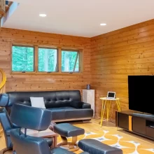 Wood-paneled living room with spiral staircase, leather seating, wall-mounted TV, warm wood flooring, and large window