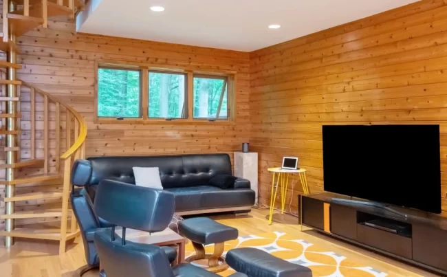 Wood Living Room with Spiral Staircase | Pennings & Sons Wood-paneled living room with spiral staircase, leather seating, wall-mounted TV, warm wood flooring, and large window