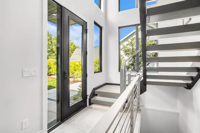 Crooked Lake Entryway with Floating Stairs | Pennings & Sons Modern entryway with black-framed glass door, floating stairs, cable railing, tall windows, and bright natural light