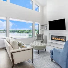 Family room with fireplace, wall-mounted TV, built-in shelves, lake-facing windows, and comfortable seating.