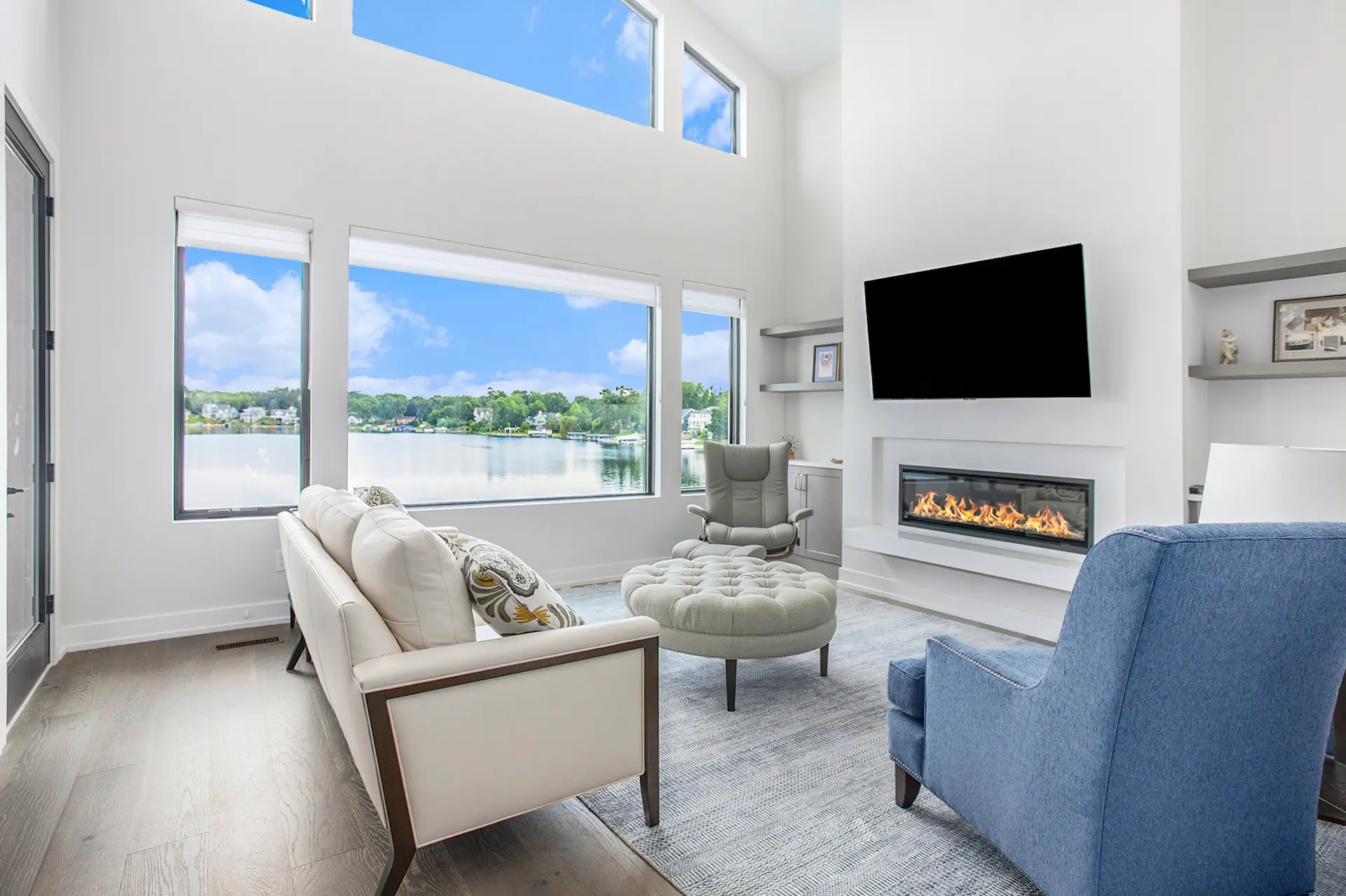 Family room with fireplace, wall-mounted TV, built-in shelves, lake-facing windows, and comfortable seating.