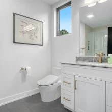 Guest bathroom with white vanity, gold hardware, gray tile floor, black door, wall mirror, and glass shower.