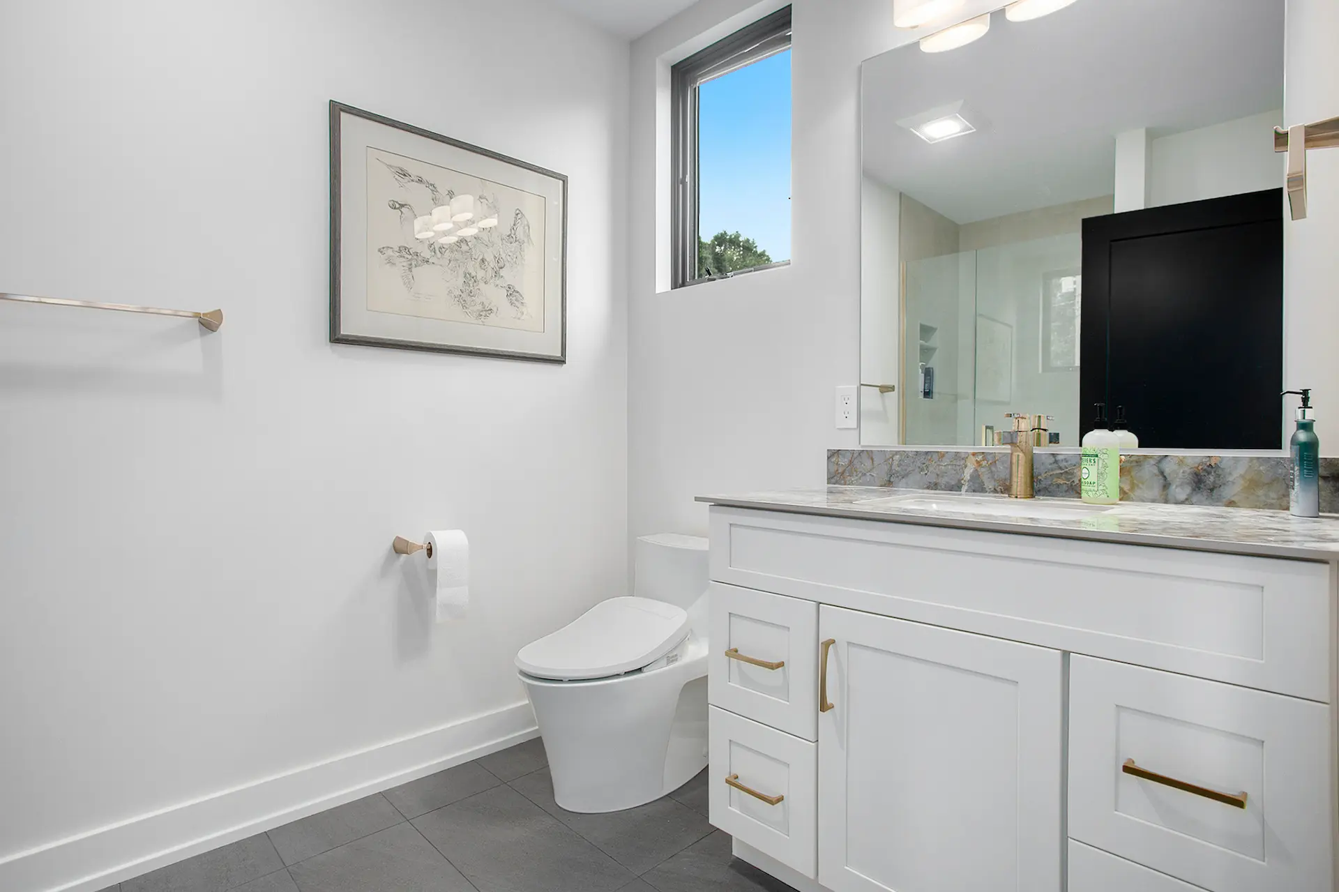 Guest bathroom with white vanity, gold hardware, gray tile floor, black door, wall mirror, and glass shower.