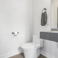 Modern half bathroom with white toilet, gray floating vanity, black faucet, wall mirror, and clean white walls.