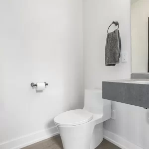 Modern half bathroom with white toilet, gray floating vanity, black faucet, wall mirror, and clean white walls.