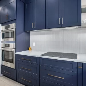Custom kitchen with navy cabinets, stainless steel appliances, built-in ovens, white countertop, and tile backsplash.