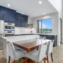 Custom kitchen with navy cabinetry, large white island, dining table extension, stainless appliances, and lake-facing windows.