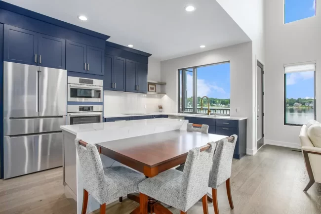 Crooked Lake Kitchen with Island | Pennings & Sons Custom kitchen with navy cabinetry, large white island, dining table extension, stainless appliances, and lake-facing windows.