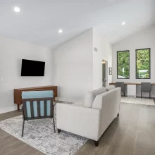 Bright loft view of a Crooked Lake living room with tall lake-facing windows, modern fireplace, wall-mounted TV, lounge chair, built-in shelves, and waterfront views
