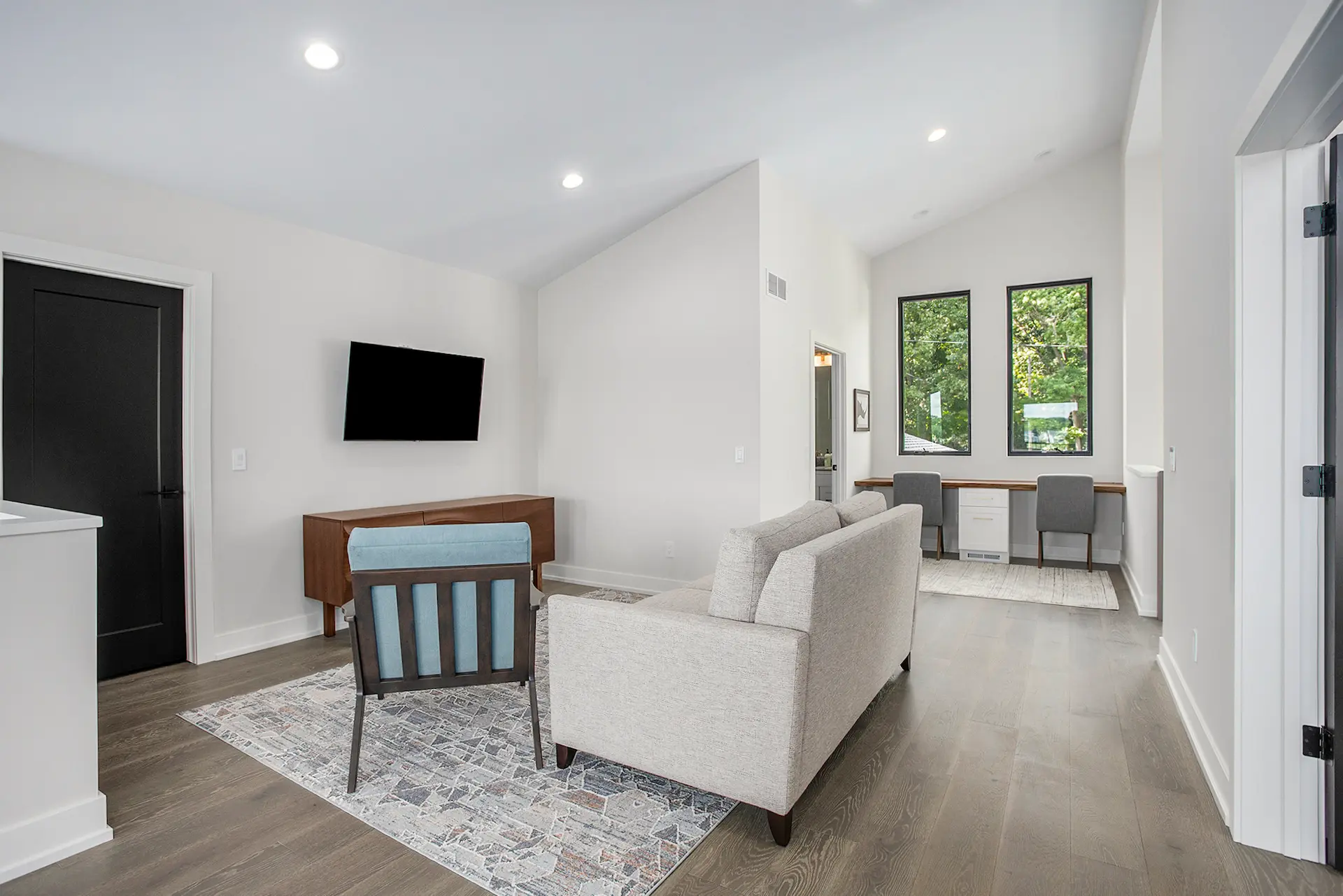 Bright loft view of a Crooked Lake living room with tall lake-facing windows, modern fireplace, wall-mounted TV, lounge chair, built-in shelves, and waterfront views