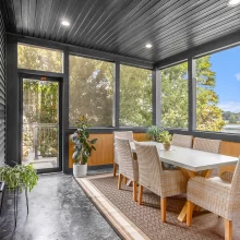Three season porch with wicker dining chairs, black screened windows, wood accent walls, potted plants, and views of Crooked Lake