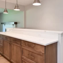 Built-in wood cabinetry with white quartz countertop, subway tile backsplash, pendant lights, and fireplace visible in adjoining room