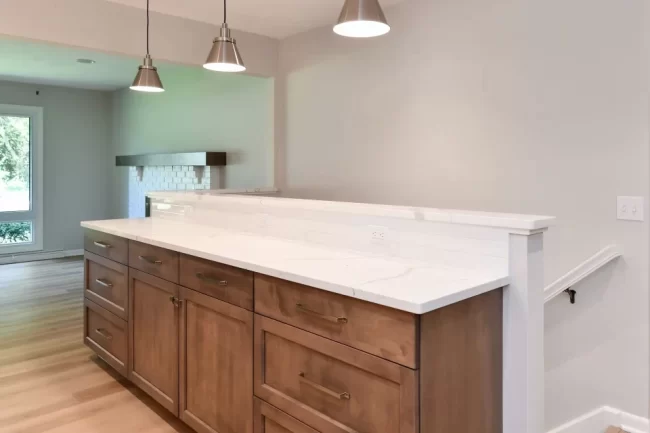 Built-In Cabinetry with Quartz Countertop | Pennings & Sons Built-in wood cabinetry with white quartz countertop, subway tile backsplash, pendant lights, and fireplace visible in adjoining room