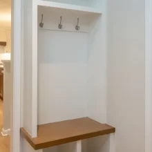 Built-in mudroom bench with wood seat, white beadboard backing, coat hooks, open cubbies, and upper storage shelves.