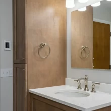 Wood bathroom vanity with tall linen cabinet, white countertop, polished nickel faucet, mirror, and three-light vanity fixture