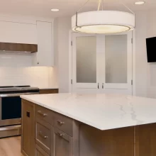 Kitchen island with wood cabinetry, white quartz countertop, large drum pendant light, white cabinets, subway tile backsplash, and stainless steel appliances