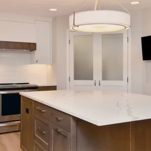 Kitchen island with wood cabinetry, white quartz countertop, large drum pendant light, white cabinets, subway tile backsplash, and stainless steel appliances