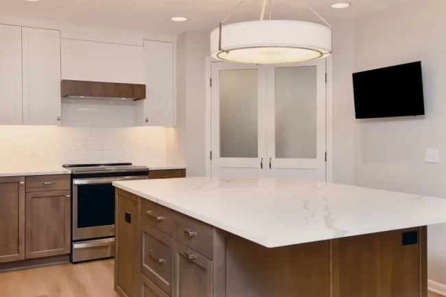 Kitchen Island with Wood Cabinets and Quartz Countertop | Pennings & Sons Kitchen island with wood cabinetry, white quartz countertop, large drum pendant light, white cabinets, subway tile backsplash, and stainless steel appliances