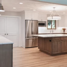 Open kitchen with wood island, white cabinets, quartz countertops, stainless steel refrigerator, pendant lights, and light wood flooring
