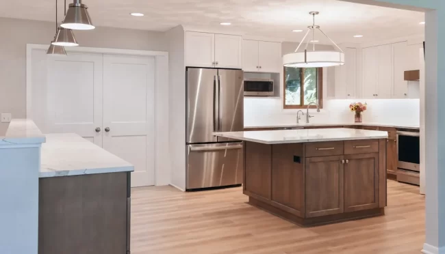 - Open kitchen with wood island, white cabinets, quartz countertops, stainless steel refrigerator, pendant lights, and light wood flooring