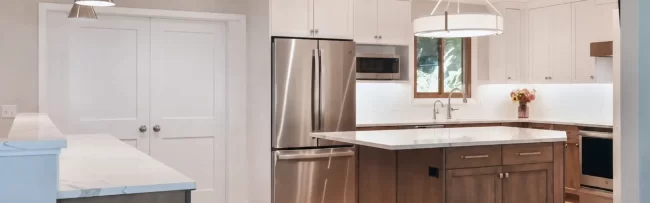 Custom Wood Island Kitchen with White Cabinets | Pennings & Sons Open kitchen with wood island, white cabinets, quartz countertops, stainless steel refrigerator, pendant lights, and light wood flooring