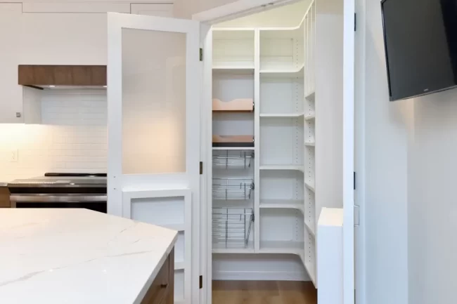 Open Kitchen Pantry with Pull-Out Shelves | Pennings & Sons Open kitchen pantry with white shelving, pull-out wire baskets, frosted glass door, and nearby quartz kitchen island