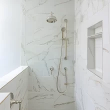 Walk-in shower with marble-look wall tile, built-in shower niche, handheld shower head, rain shower fixture, and white tile floor