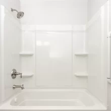 White bathtub and shower surround with built-in shelves, chrome fixtures, shower head, and wall-mounted grab bar