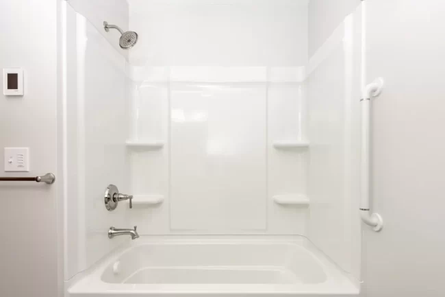 White Tub Shower Surround with Grab Bar | Pennings & Sons White bathtub and shower surround with built-in shelves, chrome fixtures, shower head, and wall-mounted grab bar