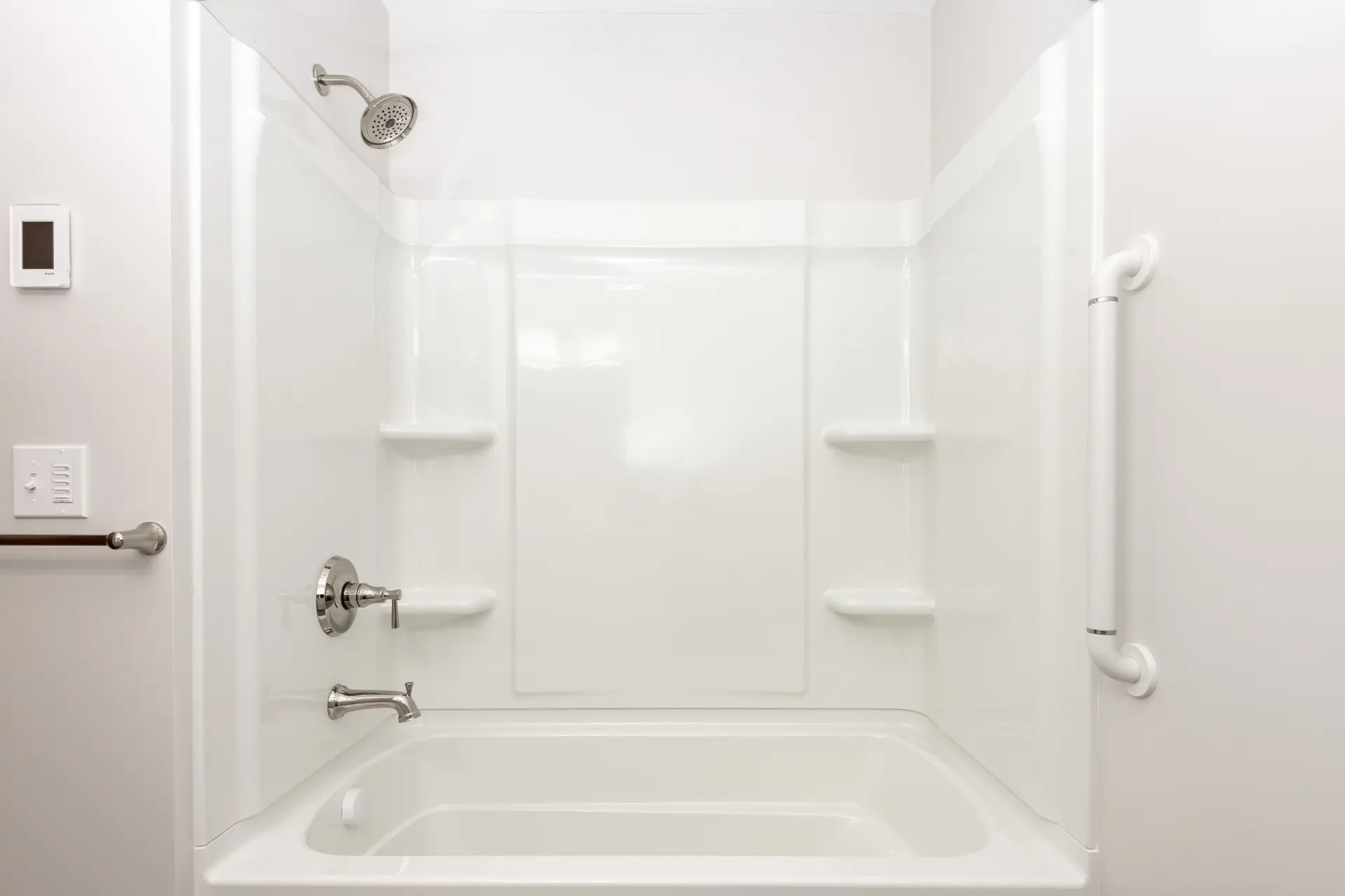 White bathtub and shower surround with built-in shelves, chrome fixtures, shower head, and wall-mounted grab bar