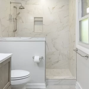 Bathroom with white marble-look tile walk-in shower, half wall, toilet, light gray floor tile, and window