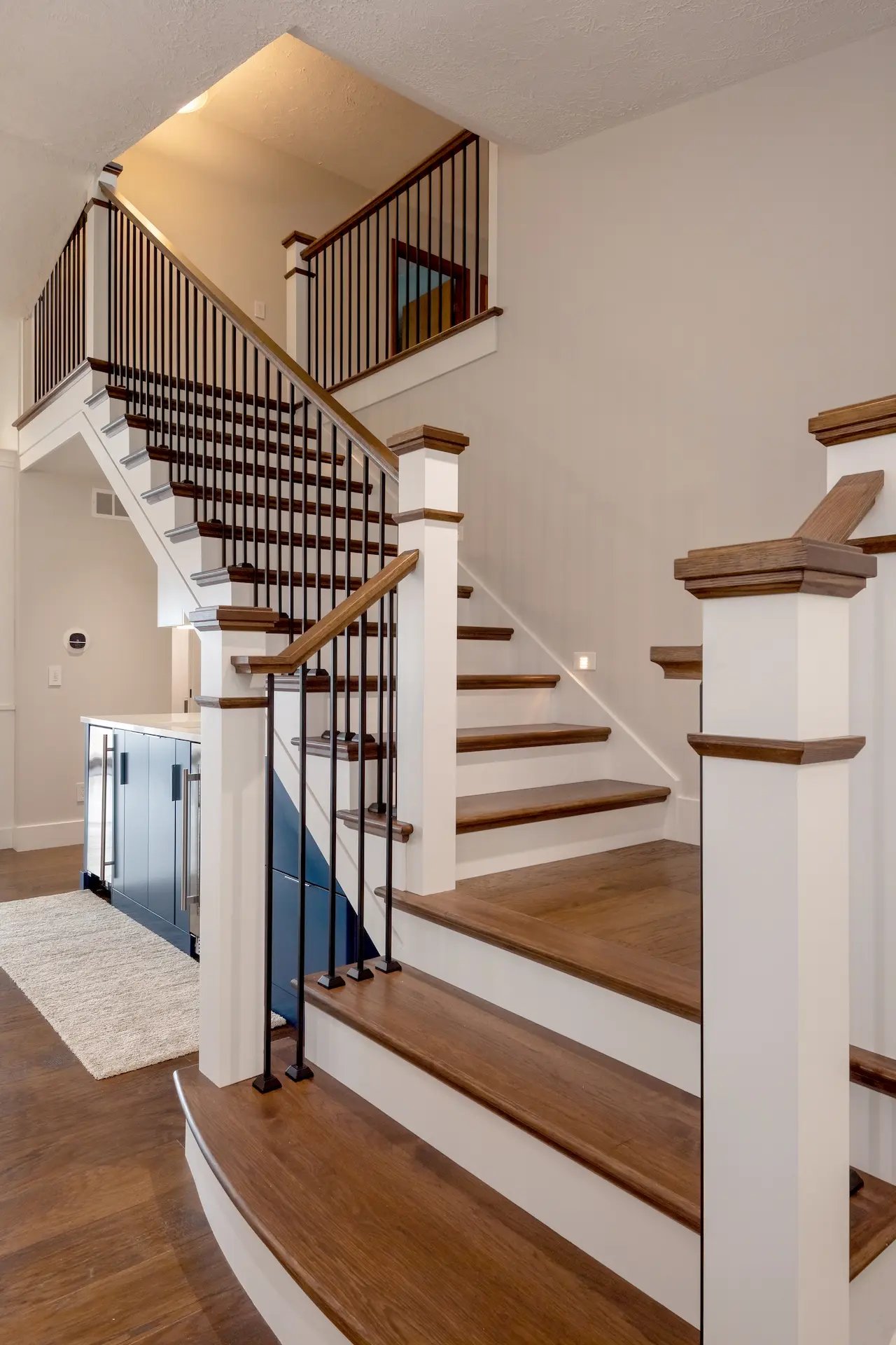 Custom wood staircase with white newel posts, dark handrails, and black iron balusters