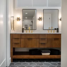 Bathroom with floating wood double vanity, gold faucets, wall sconces, black hex tile floor, and custom mirrors