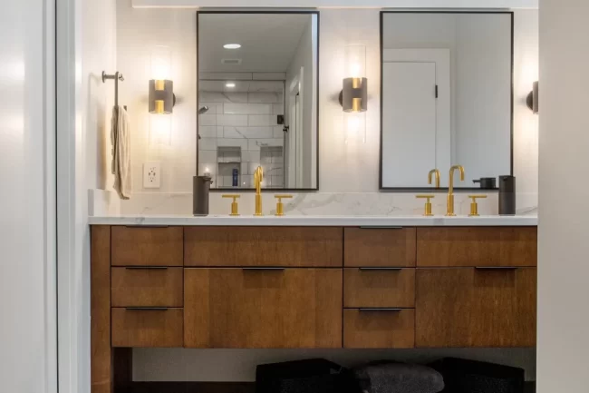 Bathroom with floating wood double vanity, gold faucets, wall sconces, black hex tile floor, and custom mirrors