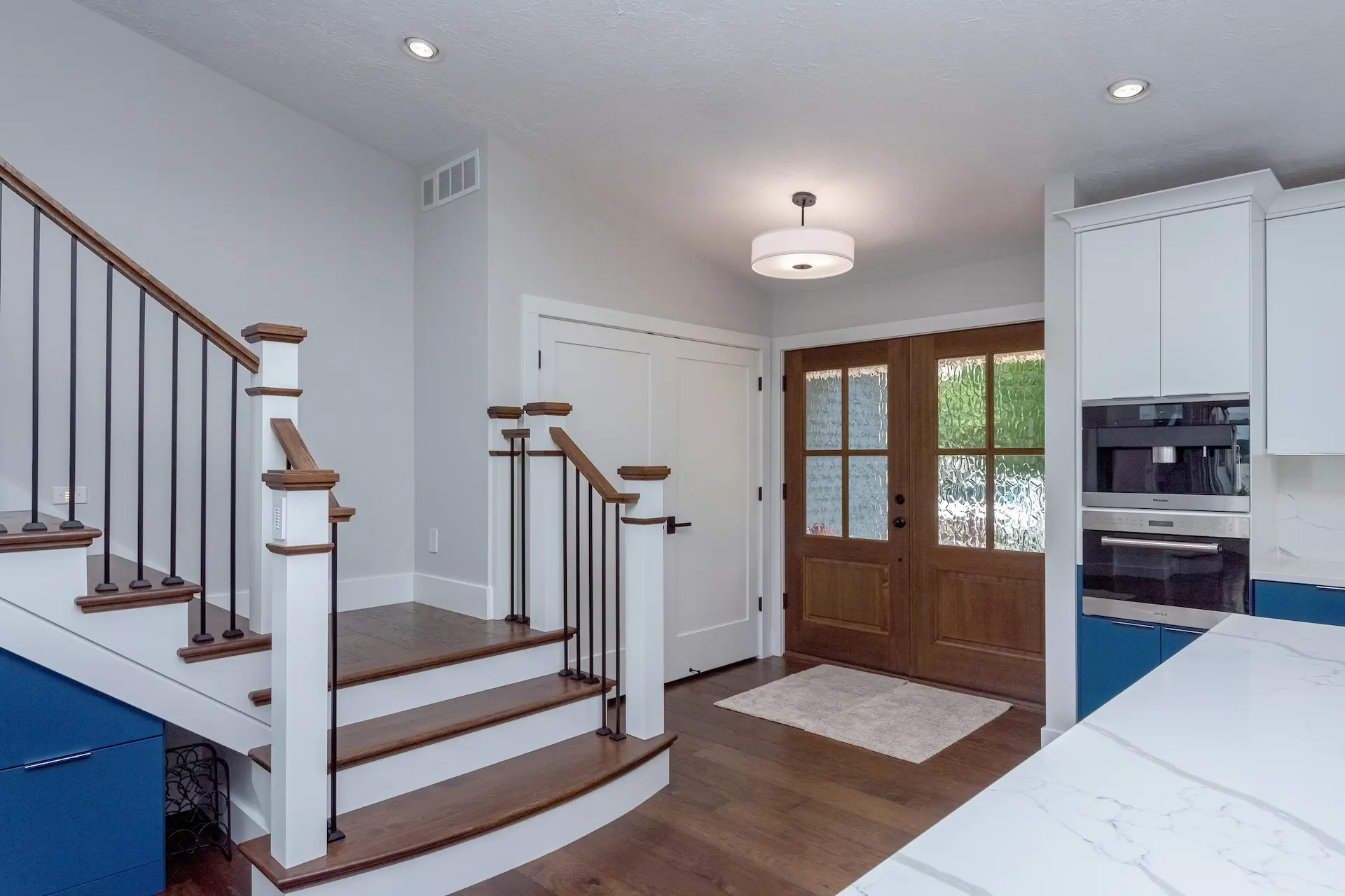 Entry staircase with wood treads, black balusters, and blue kitchen cabinetry