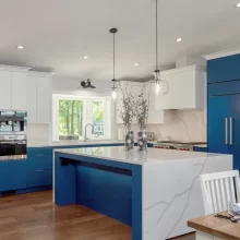 Modern blue and white kitchen with large quartz island, pendant lights, and built-in appliances