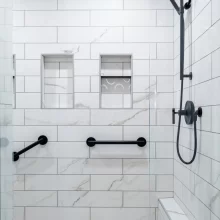 Walk-in shower with marble-look tile, glass enclosure, black fixtures, grab bars, and built-in niches