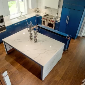 Overhead view of a blue and white kitchen with large quartz island, pendant lights, and lake home layout