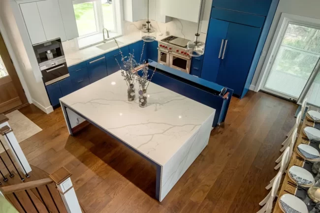 Overhead view of a blue and white kitchen with large quartz island, pendant lights, and lake home layout