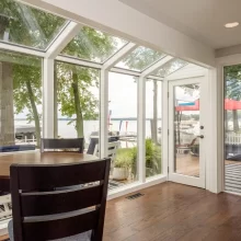 Sunroom dining area with floor-to-ceiling windows, patio door, and views of Austin Lake in Portage, MI.