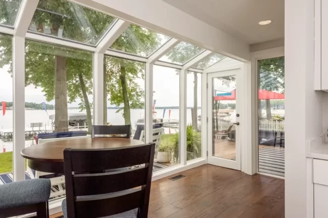 Sunroom dining area with floor-to-ceiling windows, patio door, and views of Austin Lake in Portage, MI.
