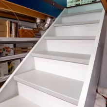 White under-stair storage area with shelves and access stairs beneath a custom kitchen movable island