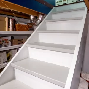 White under-stair storage area with shelves and access stairs beneath a custom kitchen movable island
