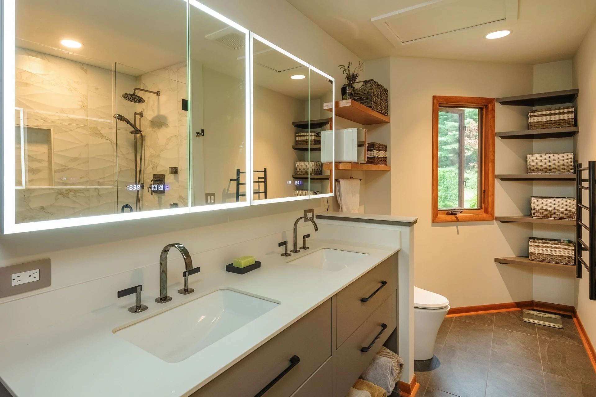 Bathroom with double vanity, lighted mirrors, open shelving, woven baskets, tile floor, and glass shower reflection