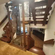 Custom home elevator shown from the hallway with wood stairs, glass enclosure, and coordinated railing design.