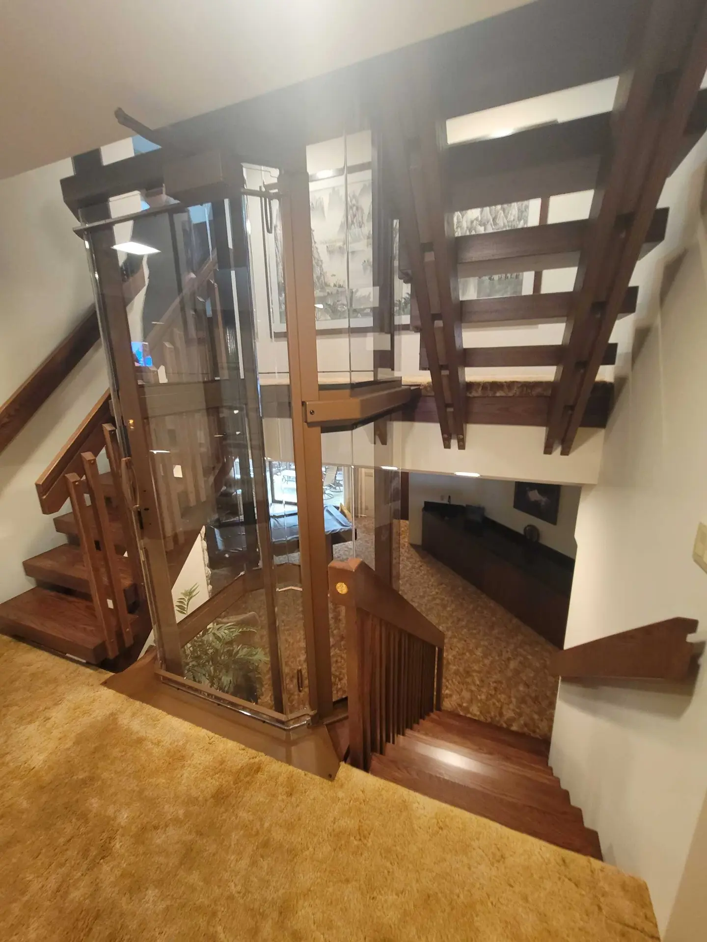 Custom home elevator shown from the hallway with wood stairs, glass enclosure, and coordinated railing design.